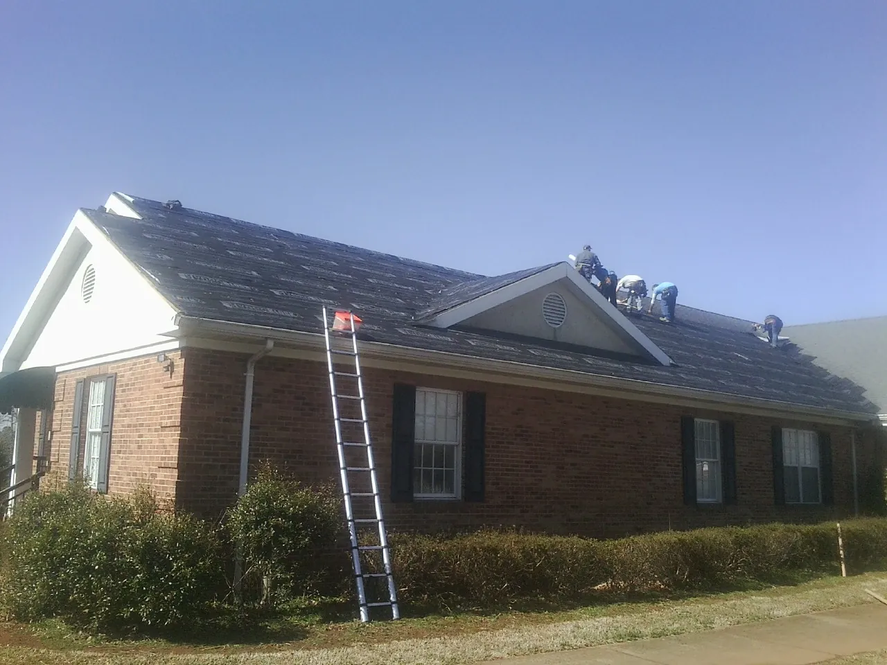 Crew tearing shingles off a brick ranch roof with a ladder set — Metal Roof Repair work by our crew in Concord